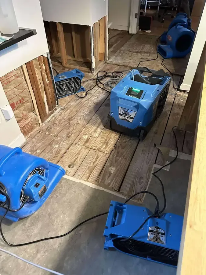 Air movers and a dehumidifier drying an opened wall and subfloor